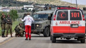 A Palestinian ambulance first responder speaks with Israeli soldiers blocking a road at a location where Palestinians were killed near the settlement of Elon Moreh in the occupied West Bank