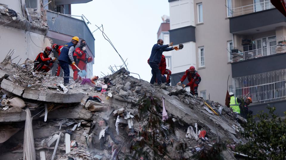 People and rescue workers stand on the rubble of a collapsed building following an earthquake in Türkiye's Adana.
