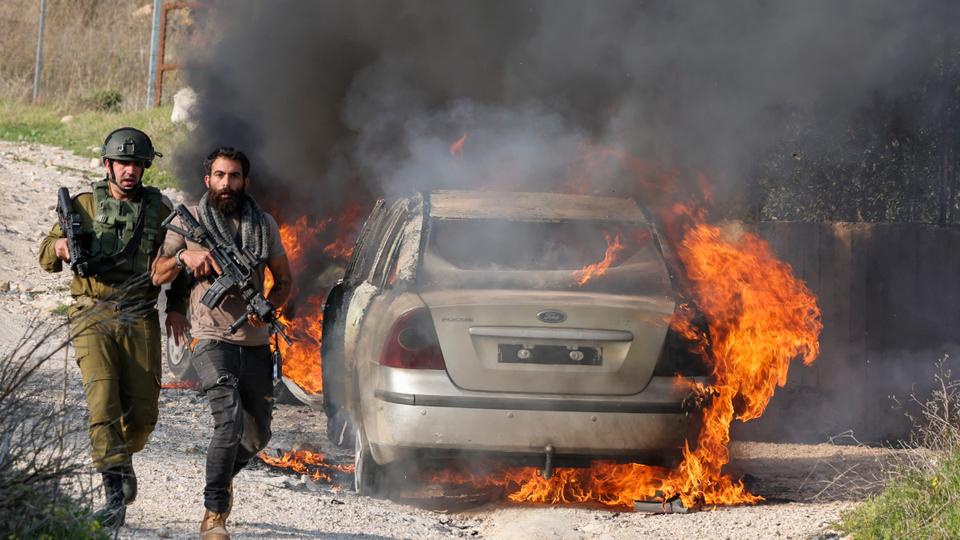 Members of Israeli forces walk past a burning car set on fire by illegal Jewish settlers from Bracha settlement, in Palestine’s Burin village in occupied West Bank.