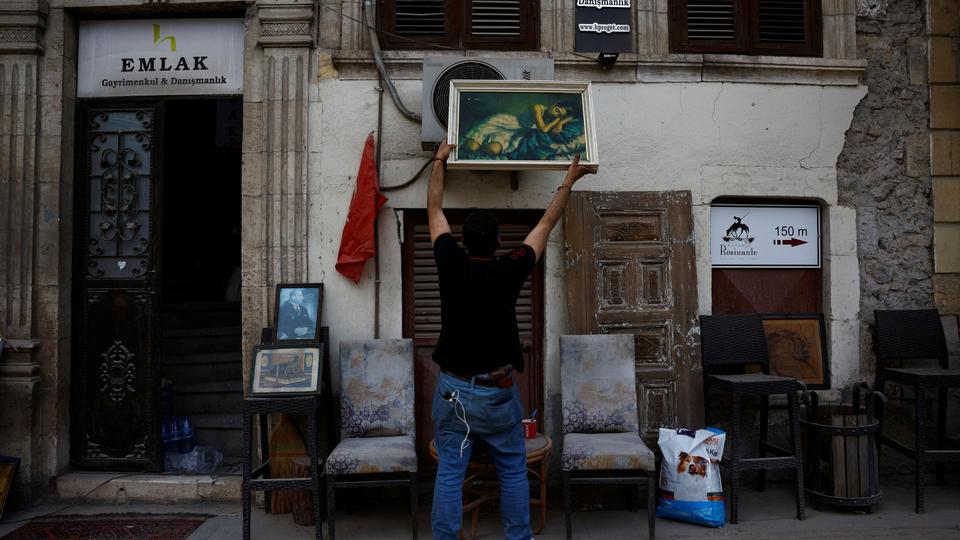 Mehmet Serkan Sincan, owner of an antique shop in central Antakya, hangs a painting outside his damaged store in the aftermath of a deadly earthquakes.