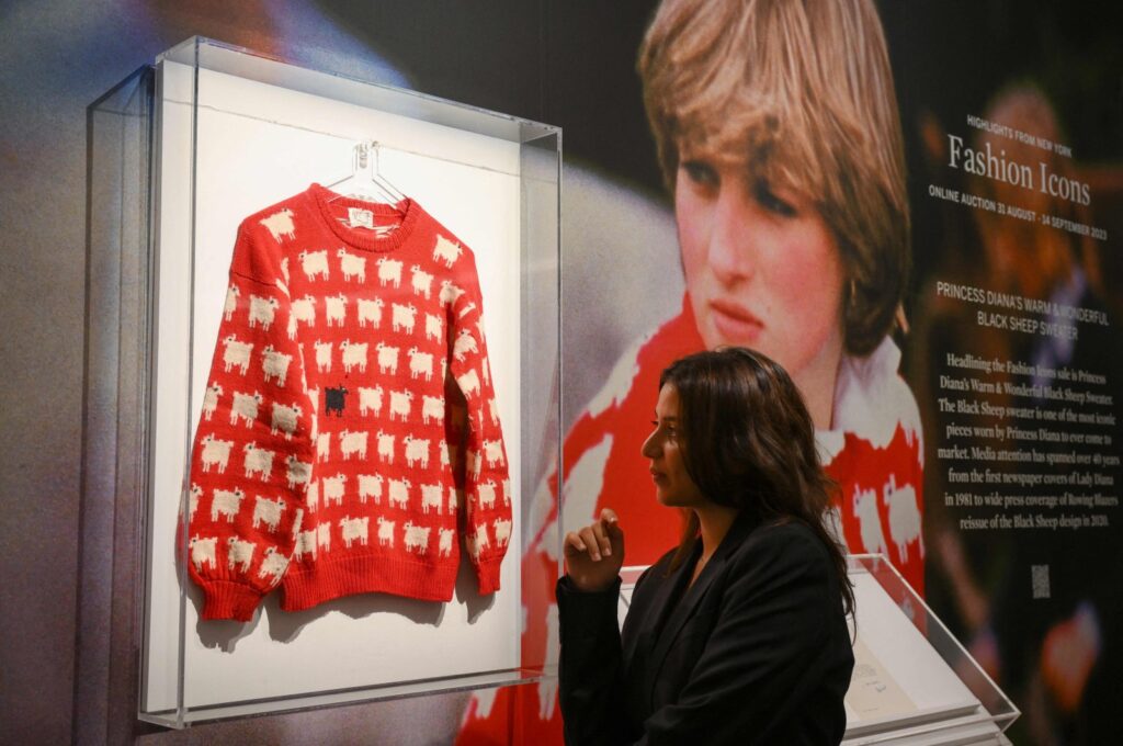 A staff member poses with the "Black Sheep Jumper" designed by Sally Muir and Joanna Osborne and worn on several occasions by Britain's late Princess Diana during a press view at Sotheby's auction house in London, U.K., July 17, 2023. (AFP Photo)