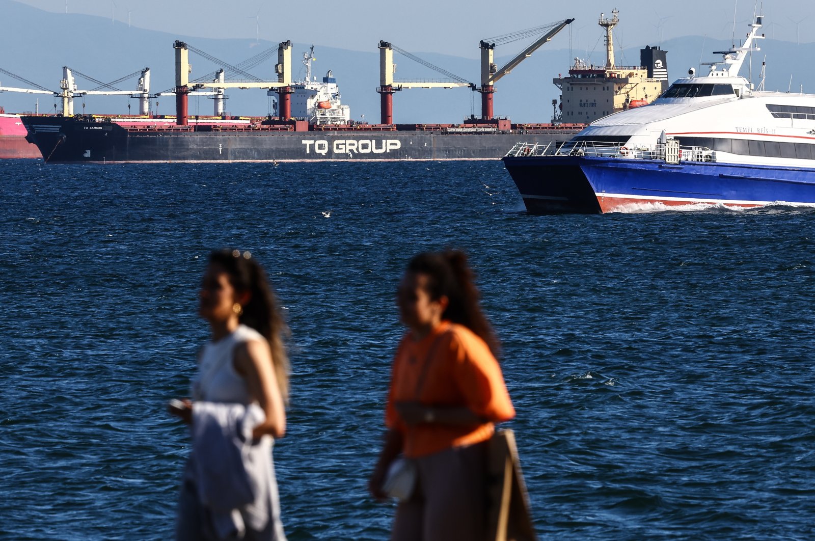 Two women pass on the river bank as the Türkiye-flagged TQ Samsunhe, the last grain ship that left a Ukrainian port since Russia exited the grain corridor agreement one day earlier, is seen in the Marmara Sea, in Istanbul, Türkiye, July 18, 2023. (EPA Photo)