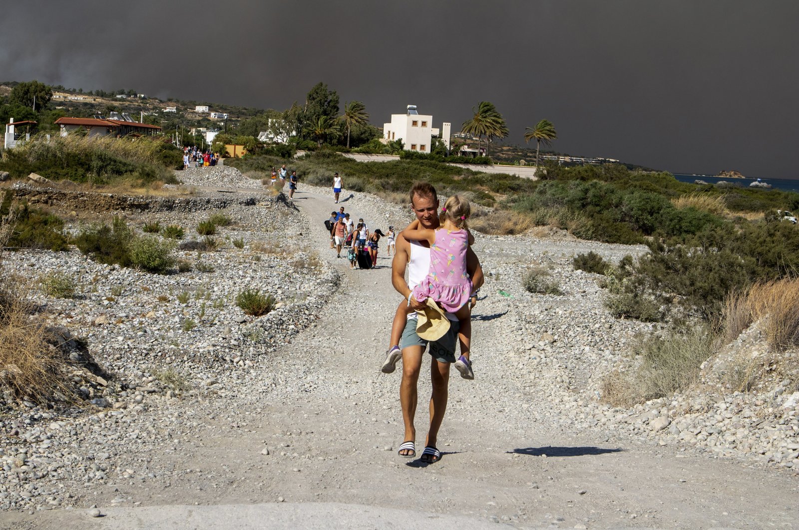 A man carries a child as they leave an area where a forest fire burns, Rhodes, Greece, July 22, 2023. (AP Photo)