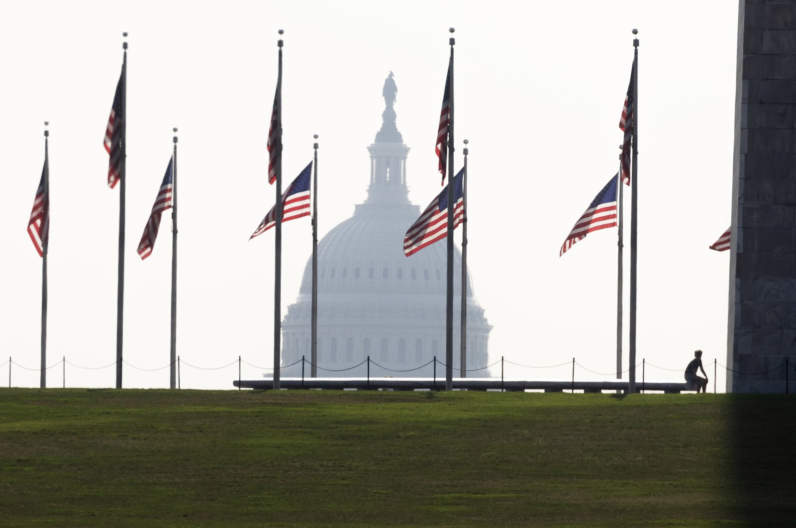 A visitor pauses at the base of the Washington Monument beneath U.S. national flags, with the U.S. Capitol seen in the background, in Washington, D.C., July 28, 2023. (EPA Photo)