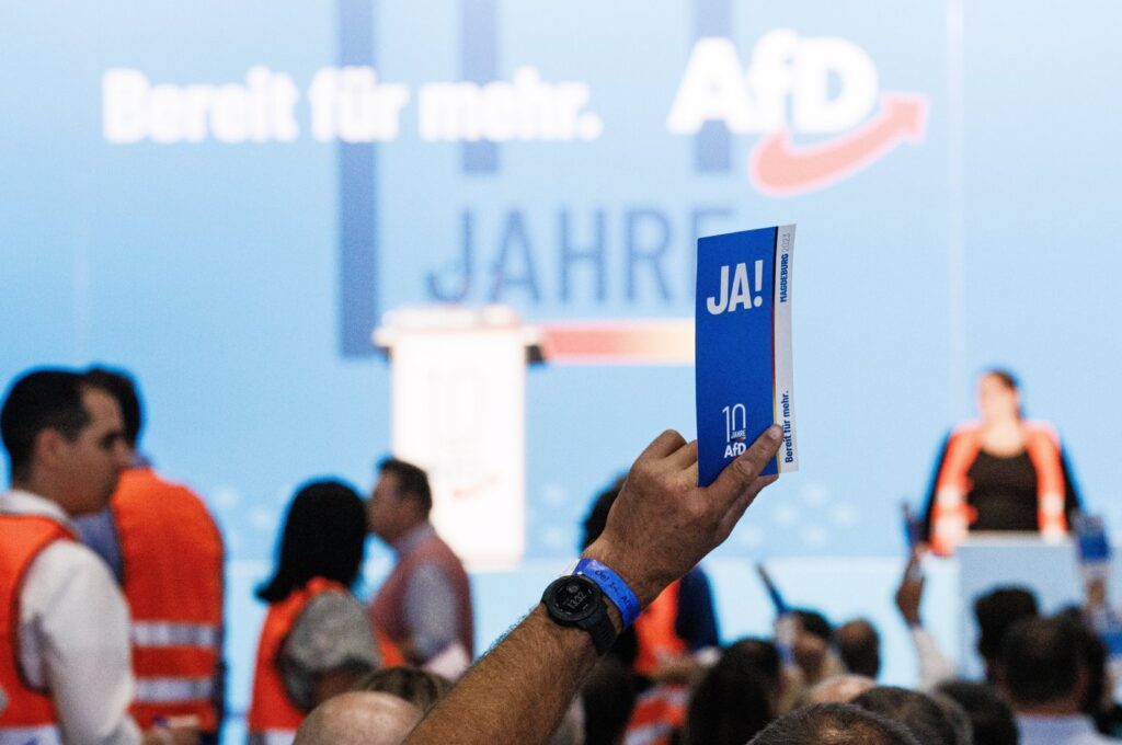 A delegate holds a voting card reading 'yes' as members of the counting committee walk in the background (orange vests) during the Alternative for Germany (AfD) party convention in Magdeburg, Germany, 28 July 2023. The Alternative for Germany (AfD) 14th federal party congress takes place in Magdeburg, July 28, 2023. (EPA Photo)