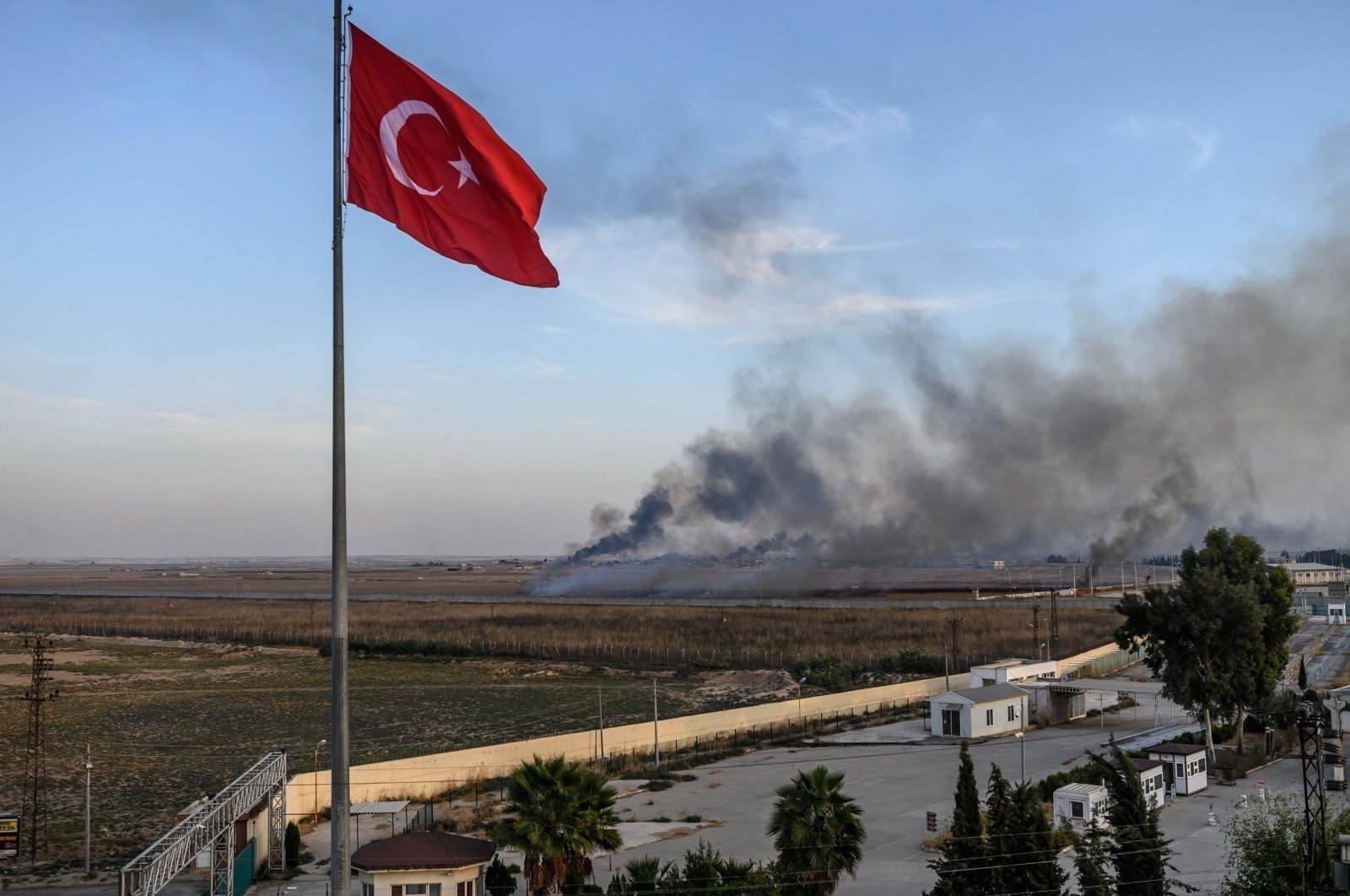 Smoke rises from the Syrian town of Tal Abyad, in a picture taken from the Turkish side of the border where the Turkish flag is seen near Akçakale, Türkiye, Oct. 10, 2019. (AFP Photo)