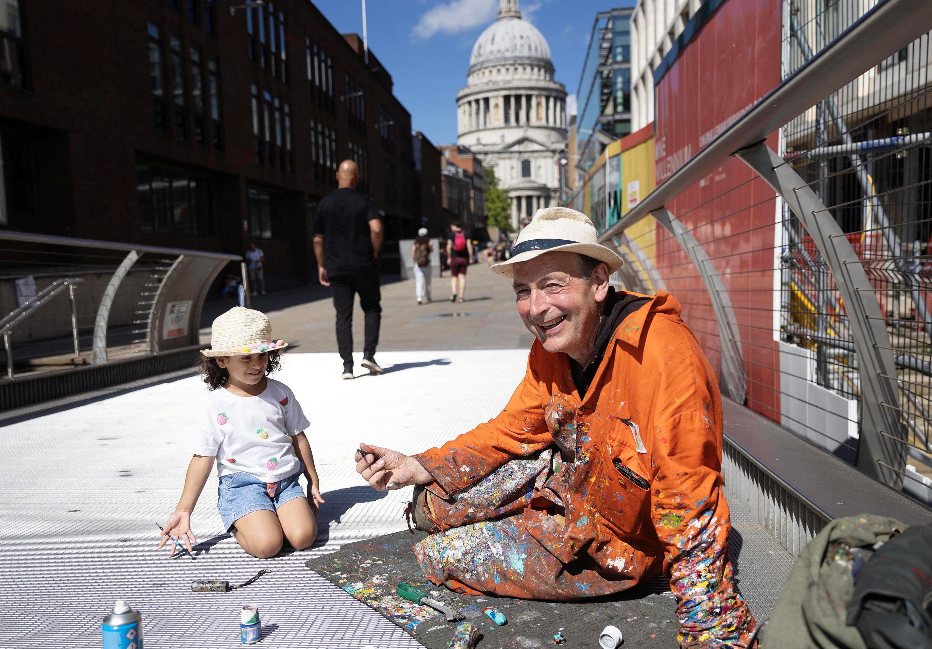 289354 Artist Ben Wilson shows Naiara, 4, how to hold a paintbrush, while he paints on the Millennium Bridge, London, U.K., Aug. 21, 2023. (Reuters Photo)