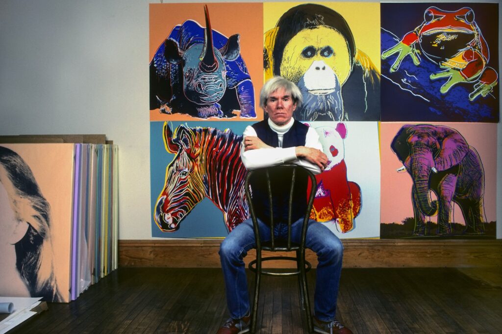 American pop artist Andy Warhol sits in front of several paintings in his "Endangered Species" series at his studio, the Factory, in Union Square, New York, U.S., April 12, 1983. (Getty Images Photo)