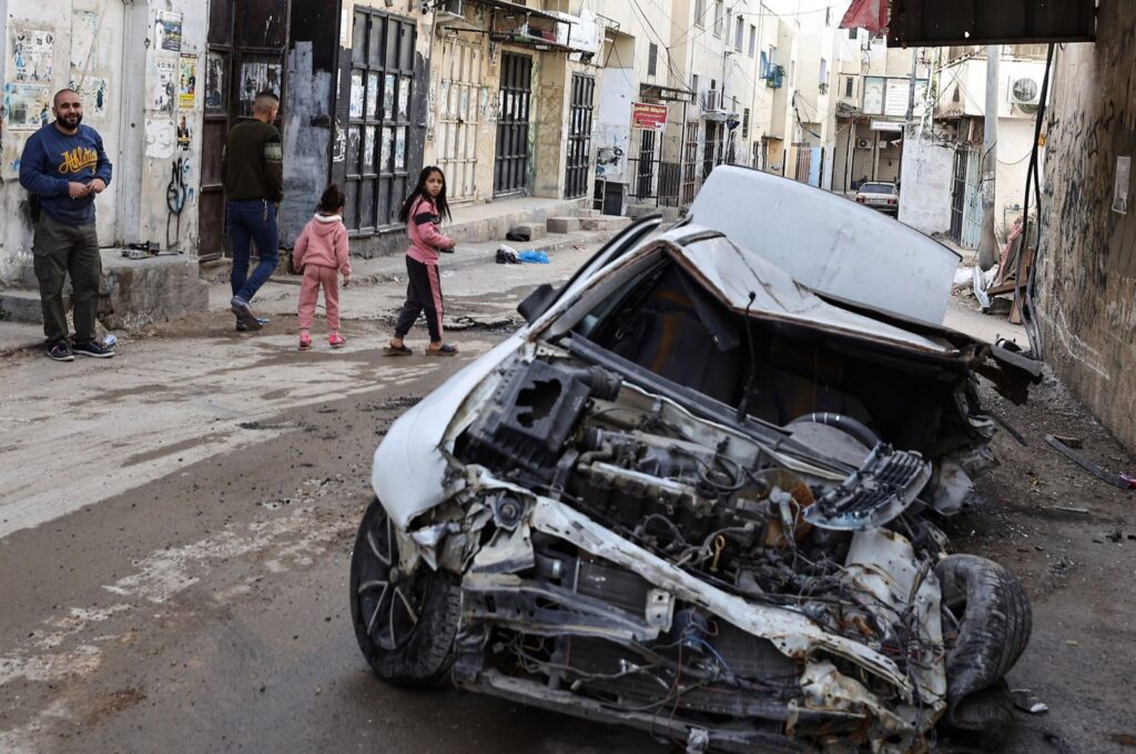 People, children walk beside a damaged car following an overnight Israeli raid in Jenin, occupied West Bank, Palestine, Nov. 26, 2023. (AFP Photo)