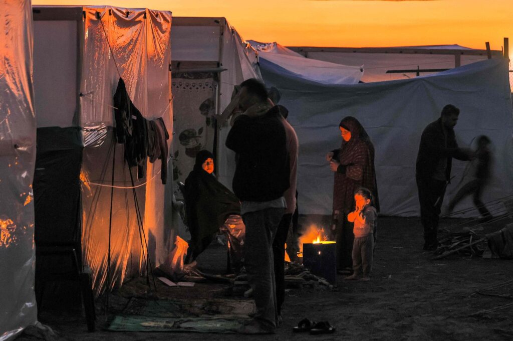 Men pray at sunset as people sit by a fire outside one of the tents housing Palestinians displaced by Israel's ruthless attacks on Gaza Strip, Dec.18, 2023. (AFP Photo)