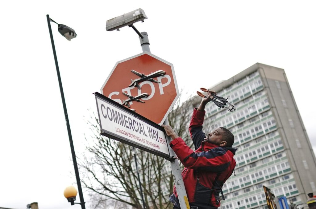 A person removes a piece of artwork by Banksy, which shows what looks like three drones on a traffic stop sign, London, U.K., Dec. 22, 2023. (AP Photo)