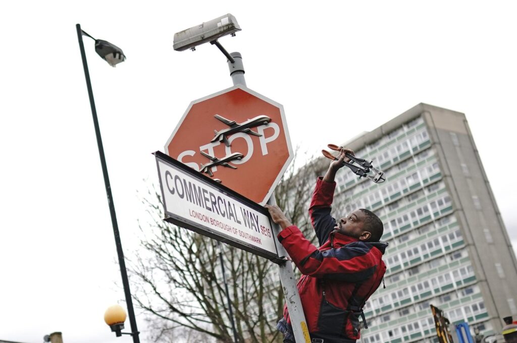 A person removes a piece of artwork by Banksy, which shows what looks like three drones on a traffic stop sign, London, U.K., Dec. 22, 2023. (AP Photo)