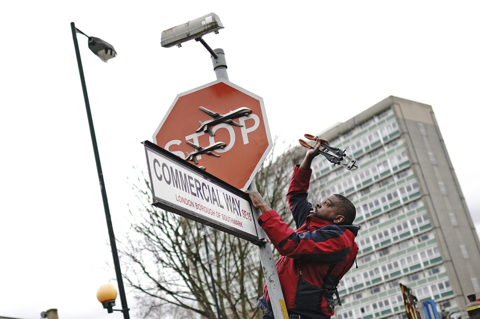 A person removes a piece of artwork by Banksy, which shows what looks like three drones on a traffic stop sign, London, U.K., Dec. 22, 2023. (AP Photo)