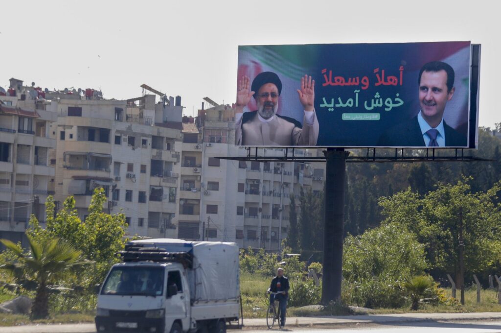 People drive under a poster with pictures of Iranian President Ebrahim Raisi (L) and Syria's Bashar Assad, in Damascus, Syria, May 3, 2023. (AP Photo)