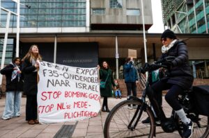 A person rides a bicycle as protesters hold placards and a banner that reads "No extra F-35 parts to Israel. Stop bombing Gaza, stop Dutch complicity," outside the court building in The Hague, Netherlands, Feb. 12, 2024. (Reuters Photo)