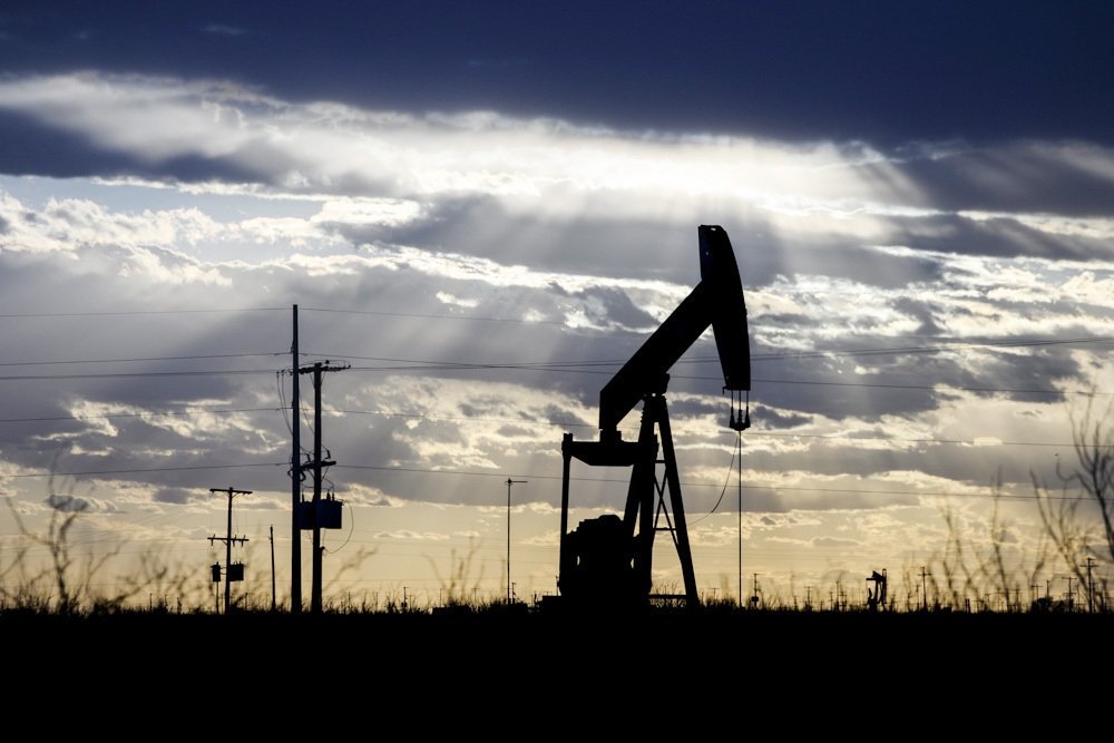 The sun shines through the clouds as it begins to set behind a pumpjack, outside of Goldsmith, Texas, U.S., March 30, 2022. (AP Photo)