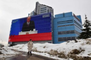 A woman walks past a screen displaying a broadcasting of Russia's President Vladimir Putin's annual State of the Nation address on the facade of a building in Moscow, Russia, Feb. 29, 2024. (AFP Photo)