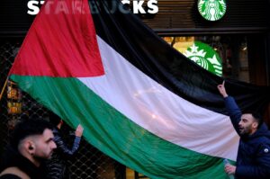 A man holds a Palestinian flag in front of a Starbucks coffee shop as people take part in a demonstration in support of Palestinians, demanding an immediate cease-fire in Gaza, Barcelona, Spain, Feb. 17, 2024. (Reuters Photo)