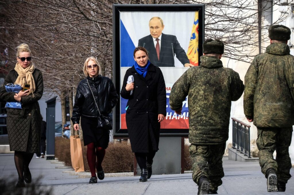 People walk in front of a poster showing Russian President Vladimir Putin and reading "The West doesn't need Russia. We need Russia!" Simferopol, occupied Crimea, Feb. 29, 2024. (AFP Photo)