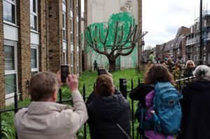 Crowds gather to view a Banksy artwork, a stencil of a person having spray painted tree foliage onto a wall behind a leafless tree, a graffiti artwork confirmed as being the work of the famous street artist near Finsbury Park in north London, U.K., March 18, 2024. (AFP Photo)