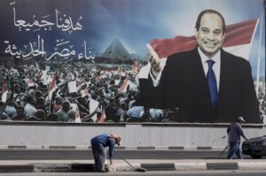 Workers clean the street under a billboard supporting Egyptian President Abdel-Fattah el-Sissi, in Cairo, Egypt, Dec. 10, 2023. (AP Photo)