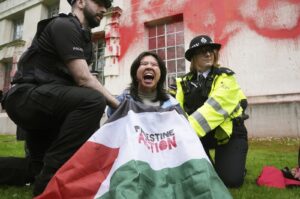 Police officers detain a person after members of Youth Demand threw red paint over the exterior of the Ministry of Defense building, London, U.K., April 10, 2024. (AP Photo)