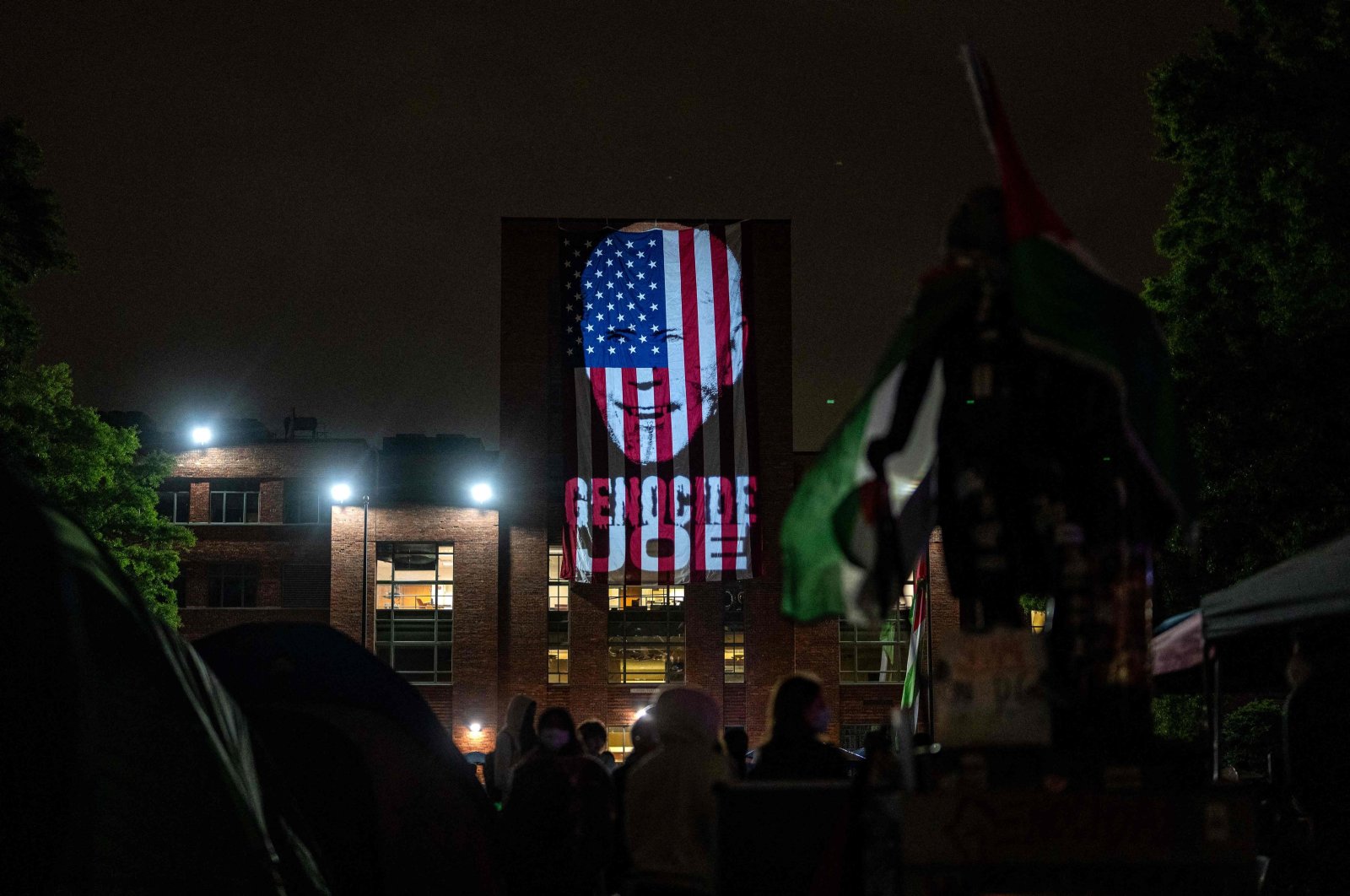 An image of President Joe Biden with the words "Genocide Joe" is projected on an American flag that hangs from GWU Law School's Lisner Hall at an encampment at University Yard at George Washington University on May 3, 2024 in Washington, D.C. (Getty Images via AFP)