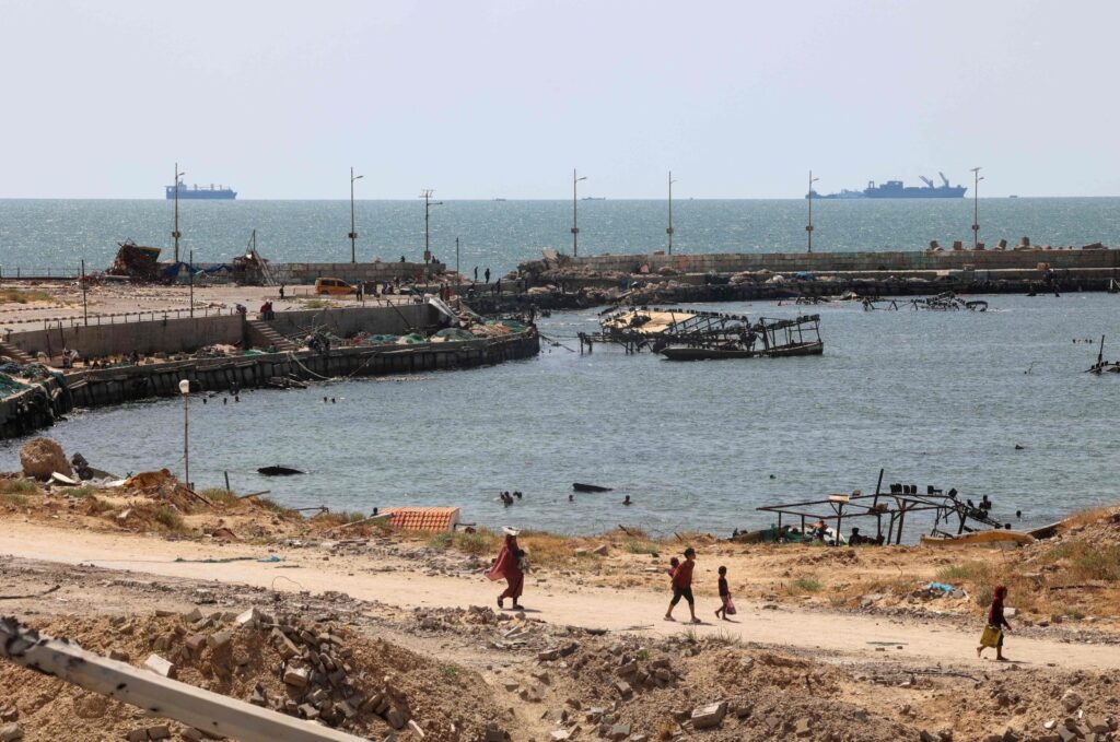 Palestinians walk past a jetty in Gaza City with a view of navy vessels off the coast as part of a humanitarian "maritime corridor" announced by U.S. Central Command (CENTCOM) May 17, 2024. (AFP Photo)
