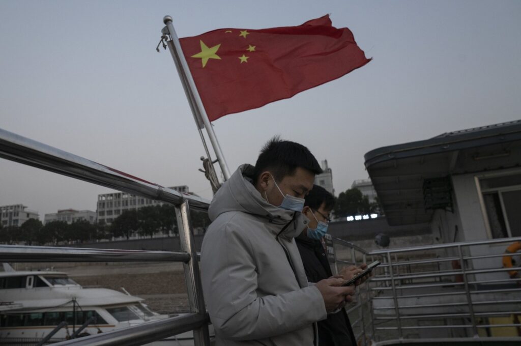 Residents taking the ferry stand near a Chinese national flag in Wuhan, in central China's Hubei province, Jan. 15, 2021. (AP Photo)