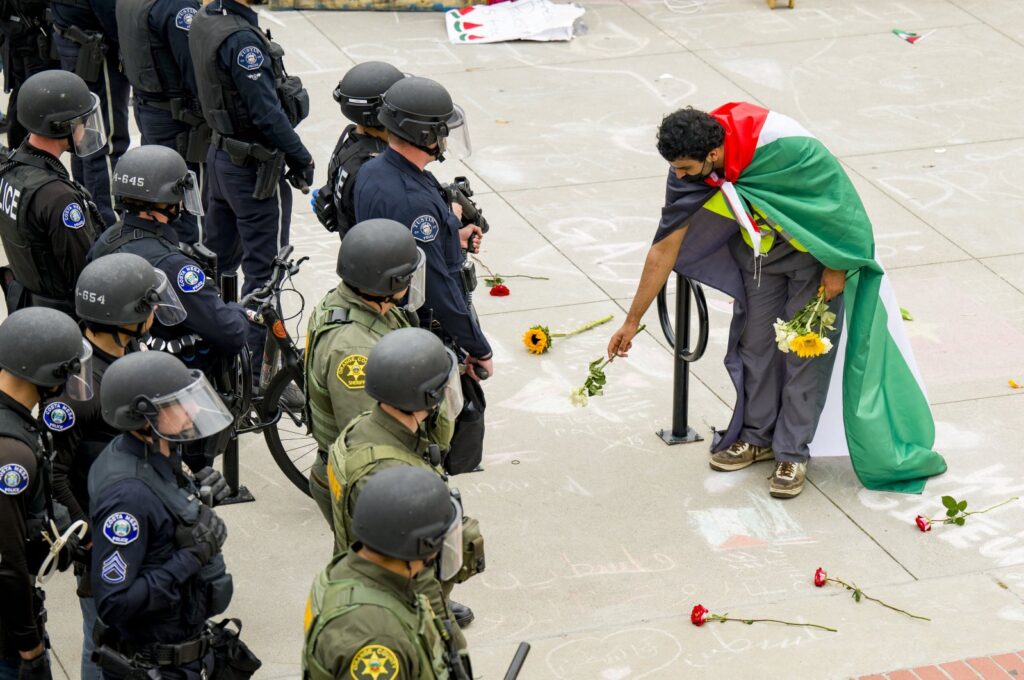 A supporter of a pro-Palestinian encampment places flowers at the feet of police at the University of California, Irvine, U.S., May 15, 2024. (AP Photo)