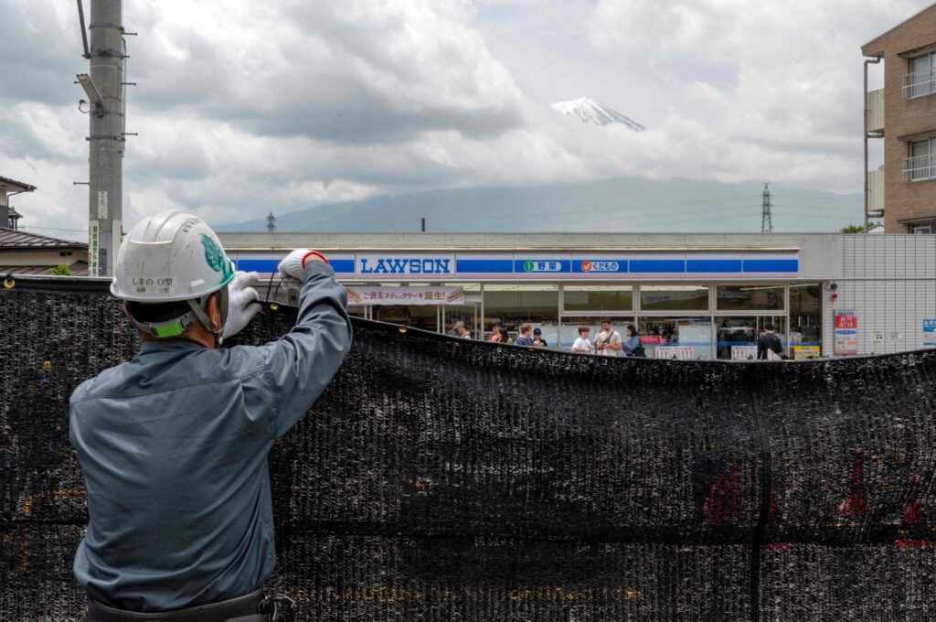 A worker installing a barrier to block the sight of Japan's Mount Fuji emerging from behind a convenience store to deter badly behaved tourists in the town of Fujikawaguchiko, Japan, May 21, 2024. (AFP File Photo)