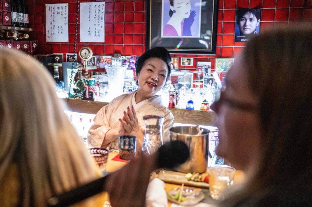 "Mama-san" Kuri Awaji (C), who runs a snack bar, claps her hands as a tourist from the U.S. (R) on a snack bar tour sings karaoke at the bar "Kuriyakko," Tokyo, Japan, March 22, 2024. (AFP Photo)