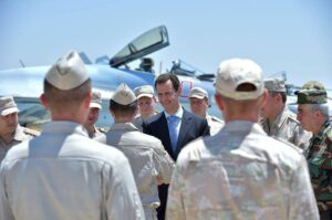 A handout picture released on the official Facebook page of the Syrian Presidency on June 27, 2017, shows President Bashar Assad (C) being welcomed by a Russian soldier during his visit to the Hmeimim military base in Latakia province, in the northwest of Syria. The Paris appealS court validated on June 26, 2024an arrest warrant for Syrian President Bashar Assad that France issued last year for alleged complicity in war crimes during Syria's civil war, according to plaintiffs lawyers. (Photo by Syrian Presidency Facebook page / AFP)