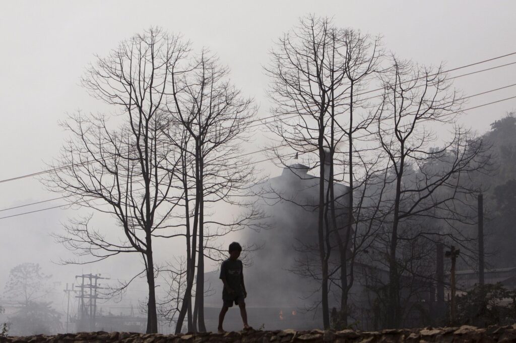 A boy walks past smoke rising from an industrial site on the outskirts of Gauhati, India, Feb. 5, 2010. (AP Photo)