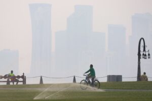 A man rides his bicycle as others sit on benches on a hot and humid summer day, in the West Bay district of Doha, Qatar, July 10, 2024. (AFP Photo)