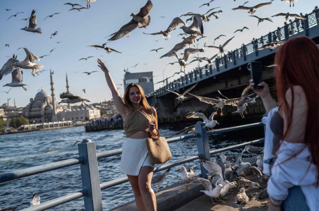 Tourists take photographs as seagulls feed on the Galata Bridge opposite the Yeni Mosque in the Karaköy neighborhood of Istanbul, Türkiye, Aug. 6, 2024. (AFP Photo)