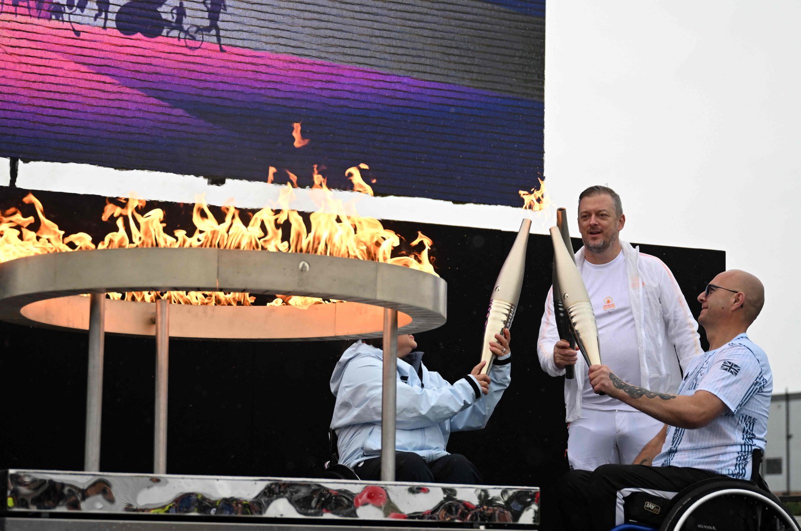 Britain's Helene Raynsford (L) and Britain's Gregor Ewan, light the torch of International Paralympic Committee President Andrew Parsons (C), lit from the cauldron, during the Paralympic torch-lighting ceremony at Stoke Mandeville, Aylesbury, U.K., Aug. 24, 2024. (AFP Photo)