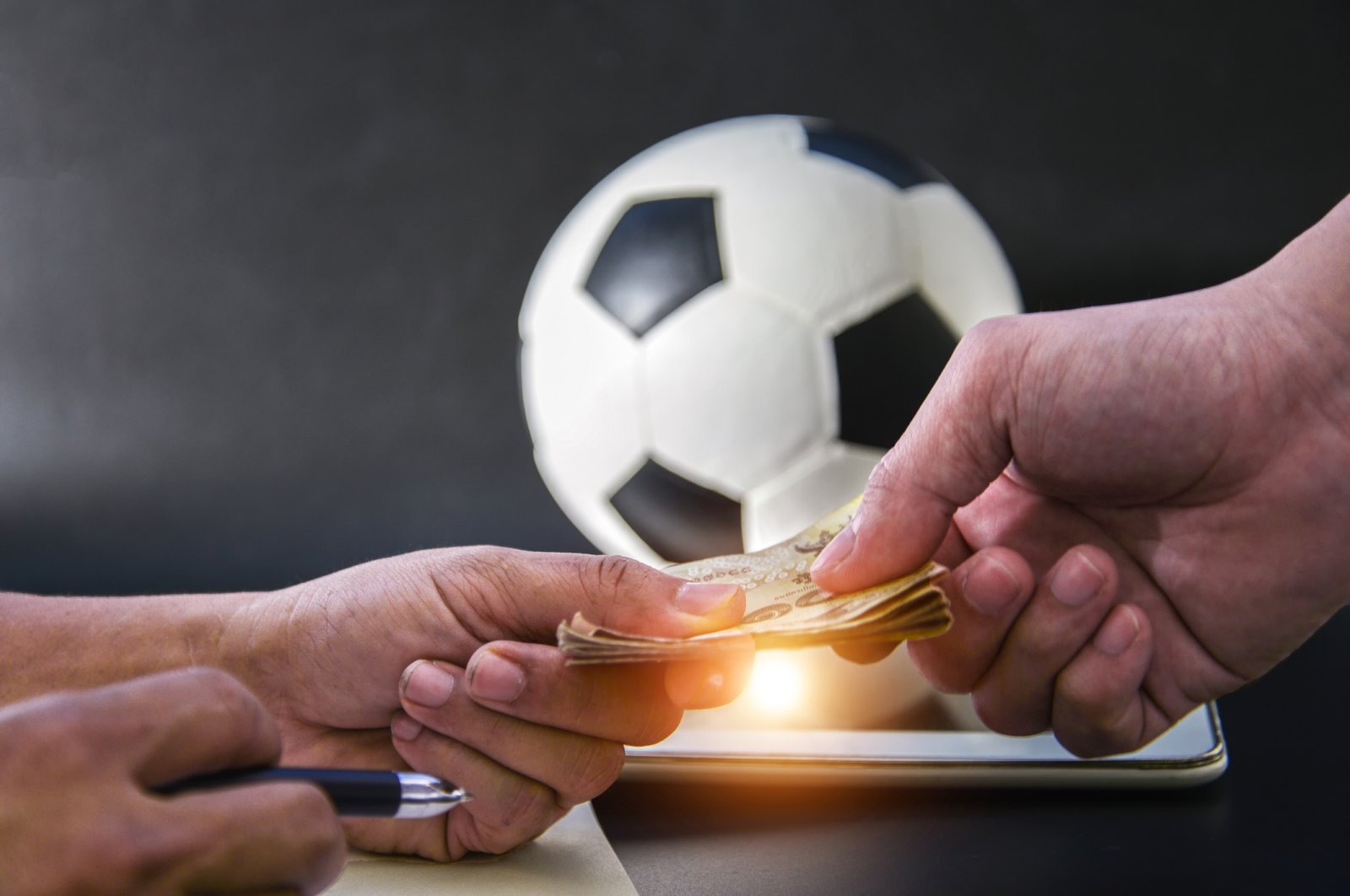 The photo shows two people exchanging money in front of a football and a tablet. (Getty Images Photo)
