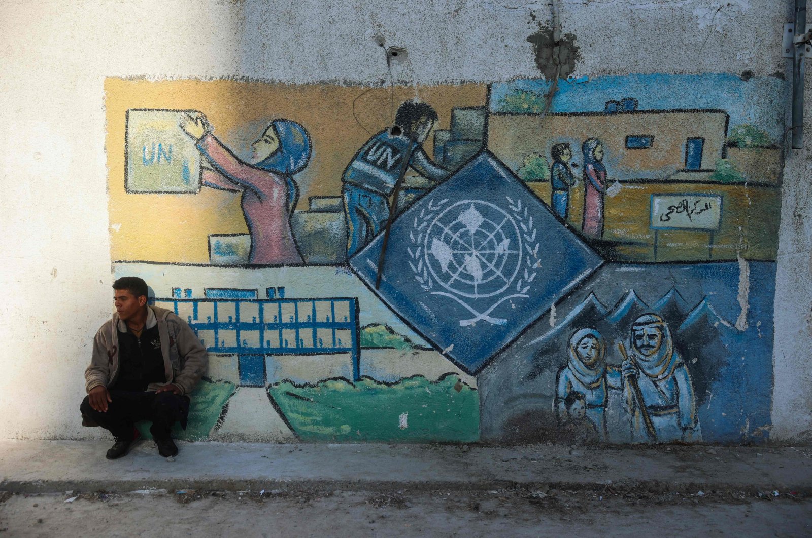 A man squats by a wall bearing a mural representing the UNRWA at the aid agency's center at the Nuseirat camp for Palestinian refugees in the central Gaza Strip, Palestine, Oct. 29, 2024. (AFP Photo)