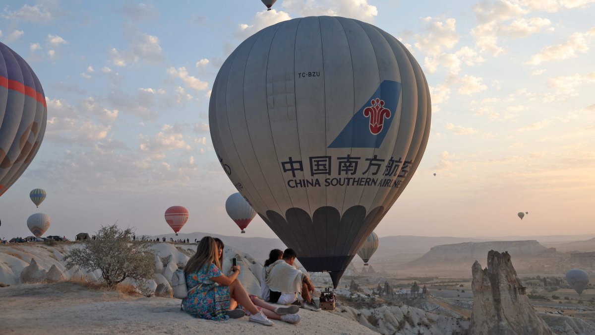 People sit along a promontory as sight-seeing hot air balloons launch in Göreme Historical National Park, east of Neveşehir in the province of the same name in central Türkiye's historical Cappadocia region, August 24, 2022. (AFP Photo)