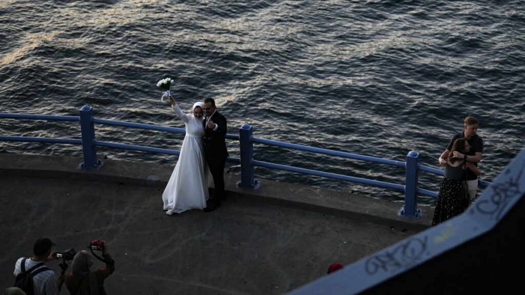 A groom and a bride pose for a photo session at Galata Bridge in Istanbul, Türkiye, July 24, 2023. (AP Photo)