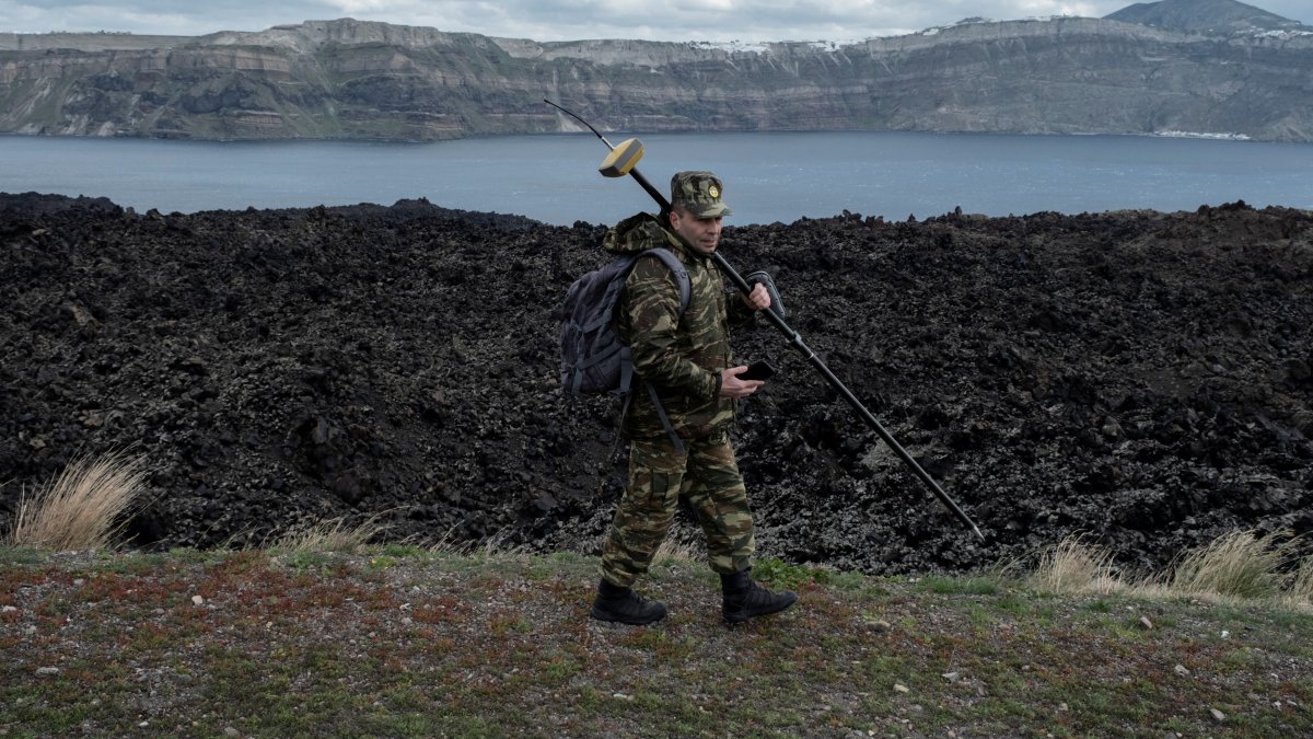 Santorini island is seen in the background as a member of Greece’s military geographical team proceeds to conduct geological measurements, to evaluate potential structural changes due to the ongoing seismic activity on the volcanic island of Nea Kameni, Greece, Feb. 10, 2025. (Reuters Photo)