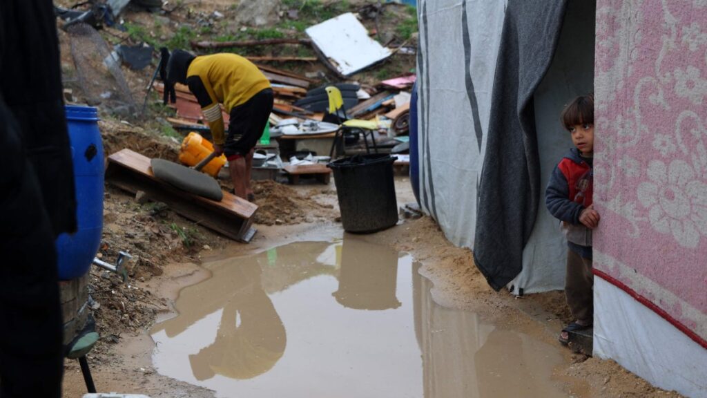 A Palestinian child stands at the entrance of a tent as a man clears the mud during the rainy season in Beit Hanoun in the northern Gaza Strip on Feb. 12, 2025. (AFP Photo)
