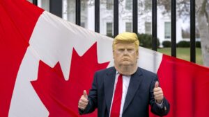 A visitor to the city wearing a mask of President Donald Trump poses for a photo in front of a Canadian flag being held by tourists from Toronto showing their support for Canada regarding trade tariffs, in front of the White House, Washington, U.S., March 13, 2025. (AP Photo)