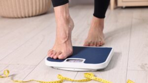 A woman stepping on a floor scale and using a measuring tape at home. (Shutterstock Photo)