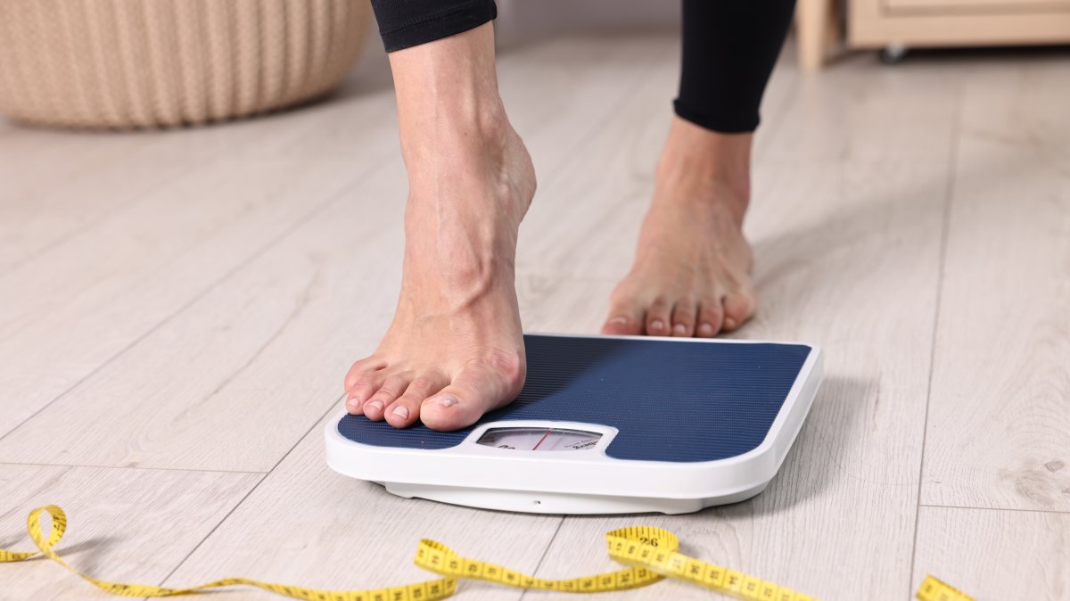 A woman stepping on a floor scale and using a measuring tape at home. (Shutterstock Photo)