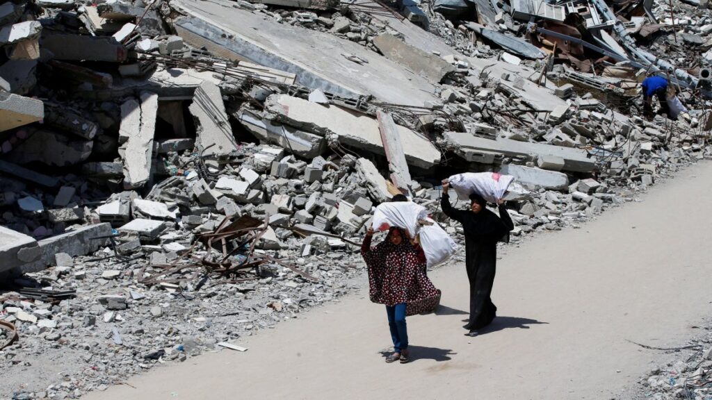 A Palestinian woman and a girl carrying bags of firewood walk by the rubble of houses, in Gaza City, Palestine, May 20, 2025. (Reuters Photo)