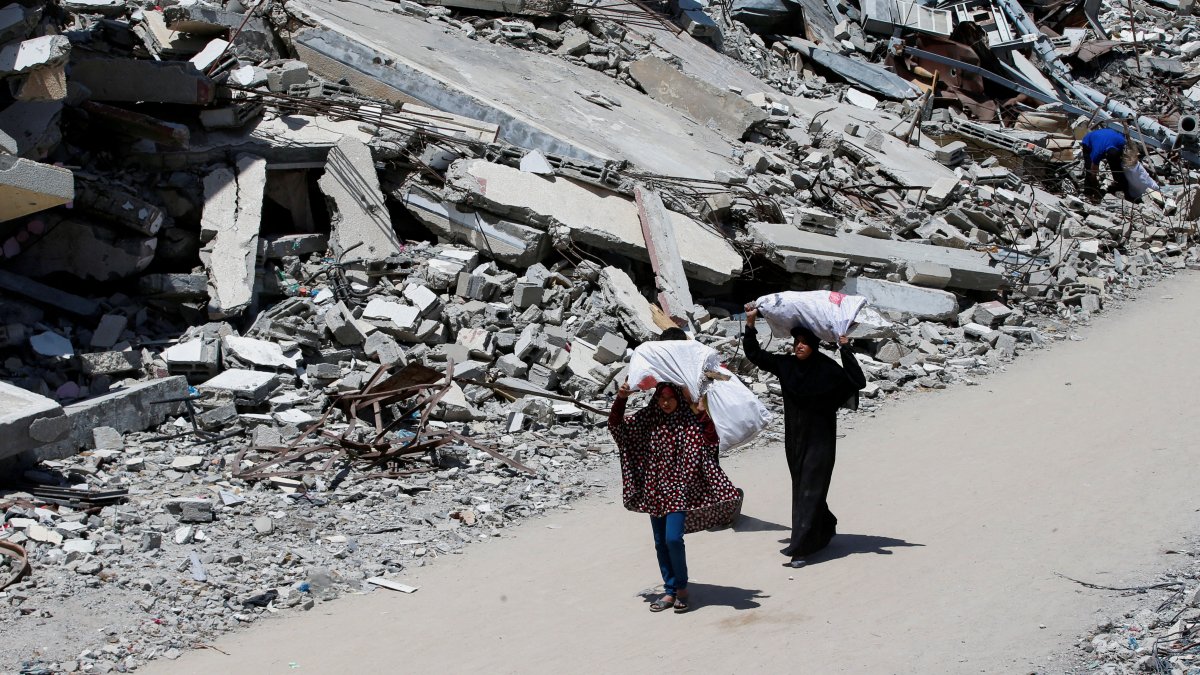 A Palestinian woman and a girl carrying bags of firewood walk by the rubble of houses, in Gaza City, Palestine, May 20, 2025. (Reuters Photo)