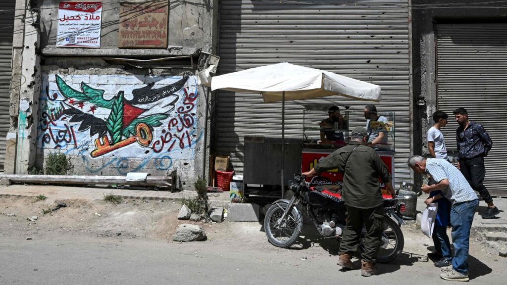 Men check a motorbike next to a mural painting bearing an image of the Syrian and Palestinian flags in the Yarmuk camp, Damascus, Syria, May 22, 2025. (AFP Photo)