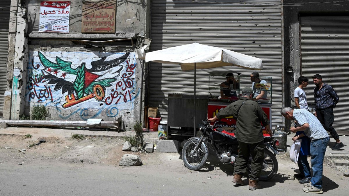 Men check a motorbike next to a mural painting bearing an image of the Syrian and Palestinian flags in the Yarmuk camp, Damascus, Syria, May 22, 2025. (AFP Photo)